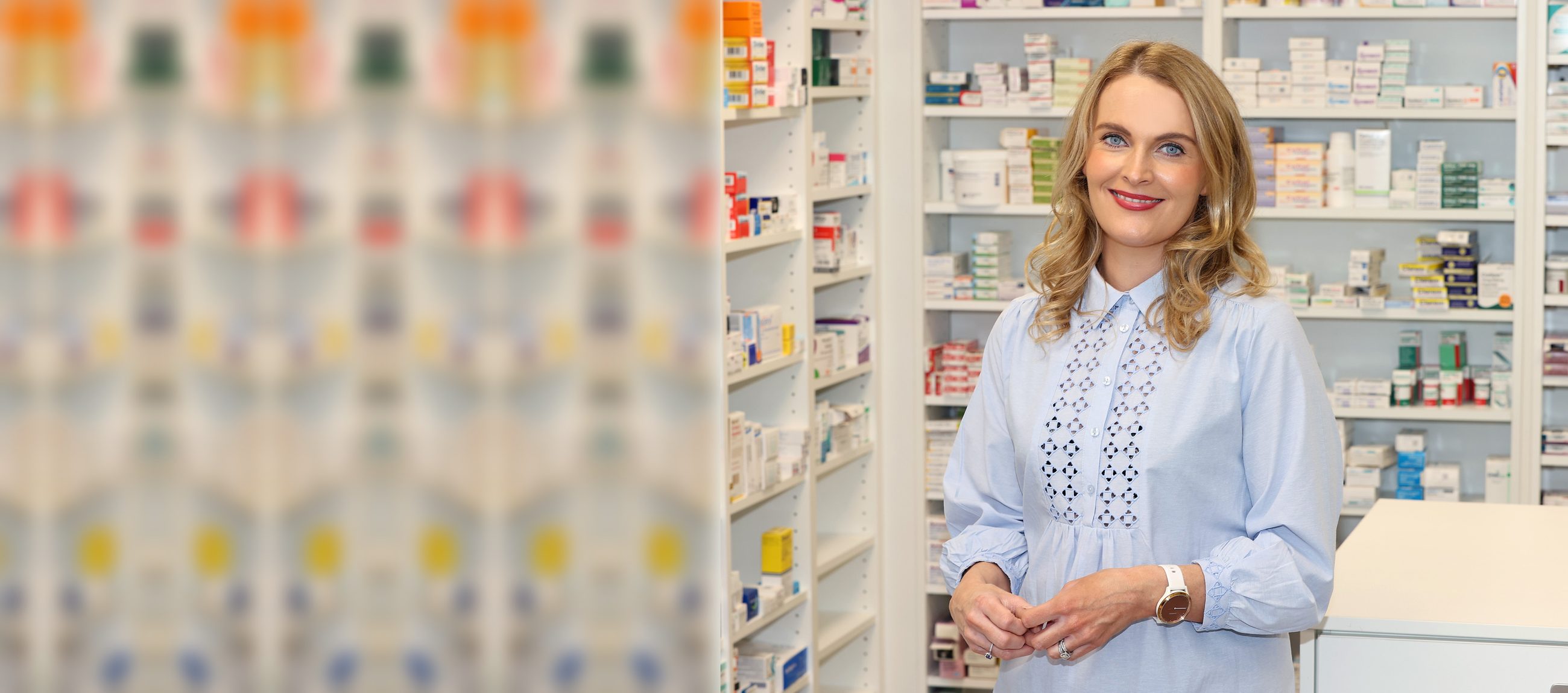 A smiling McGreals pharmacy team member standing in front of dispensary shelves